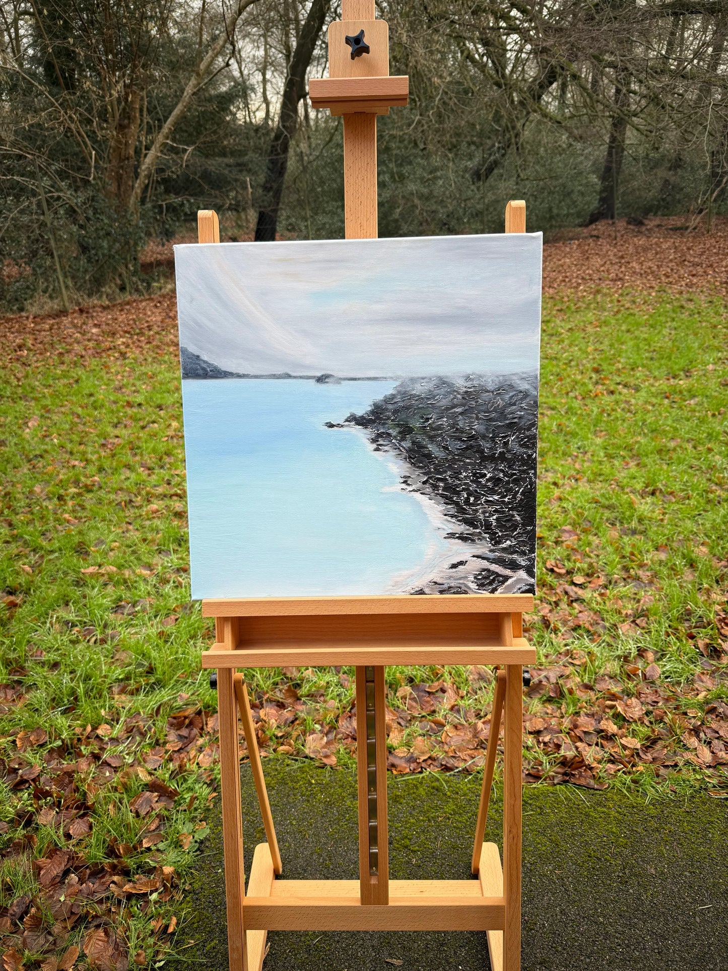 Romantic abstract seascape oil painting with blue water and rocky shoreline on an easel outdoors