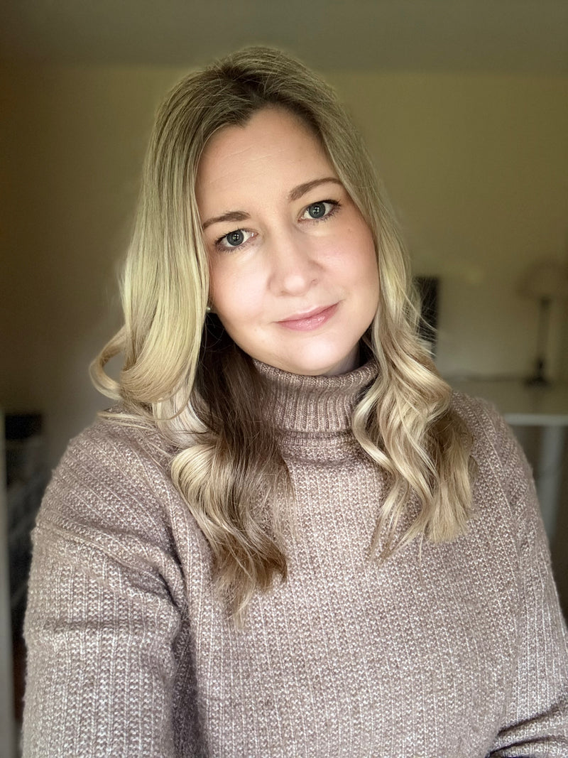 Woman with blonde hair wearing a beige turtleneck sweater indoors.