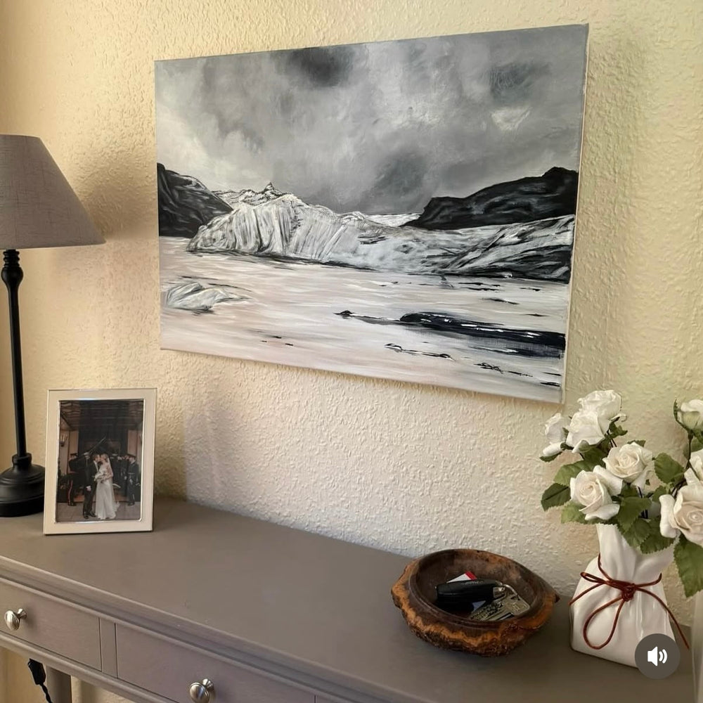 Acrylic painting of a glacier in Iceland, positioned above a grey console table with decorative items including a vase of flowers, a photo frame, and a bowl.