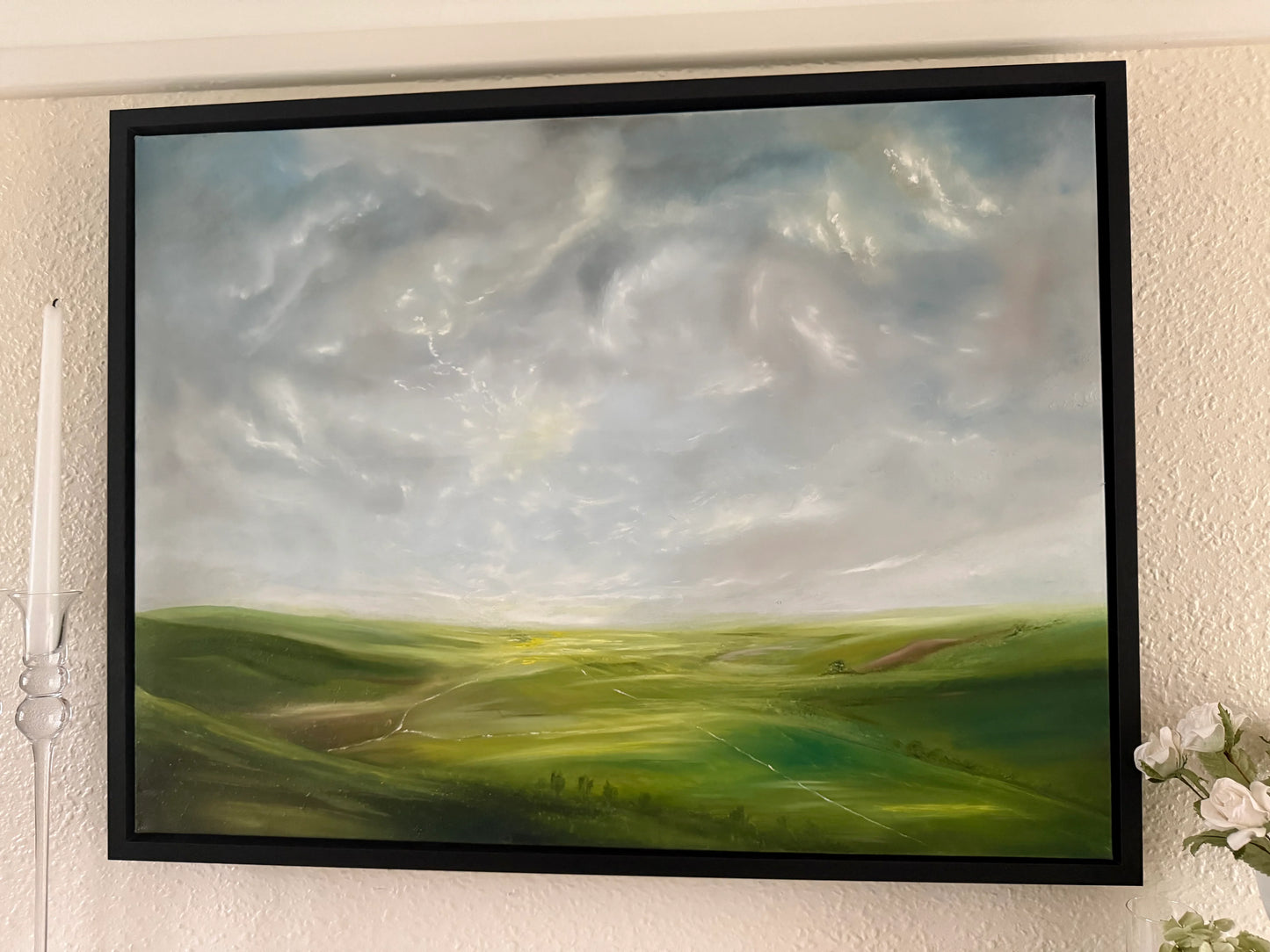 Framed romantic landscape oil painting of green rolling hills under a dramatic cloudy sky.