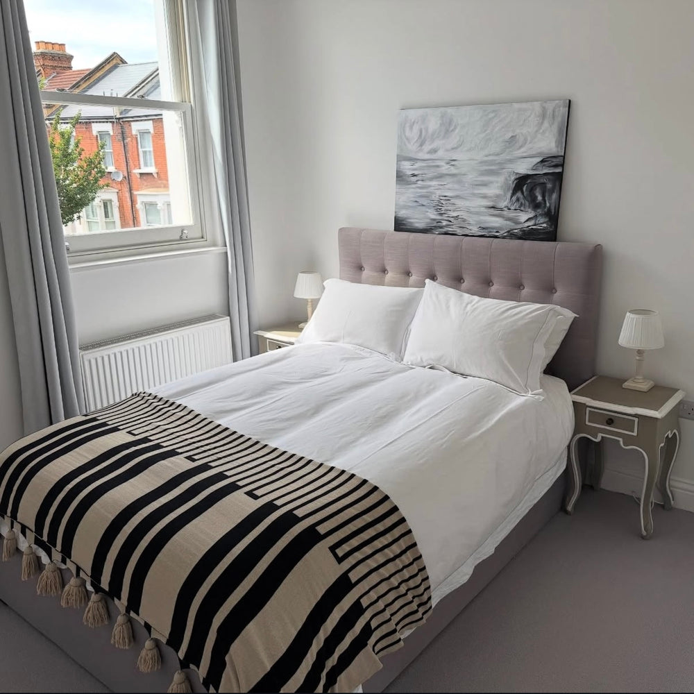 Acrylic painting of a stormy sea and cliff, in a modern bedroom with a grey upholstered bed and white bedding.