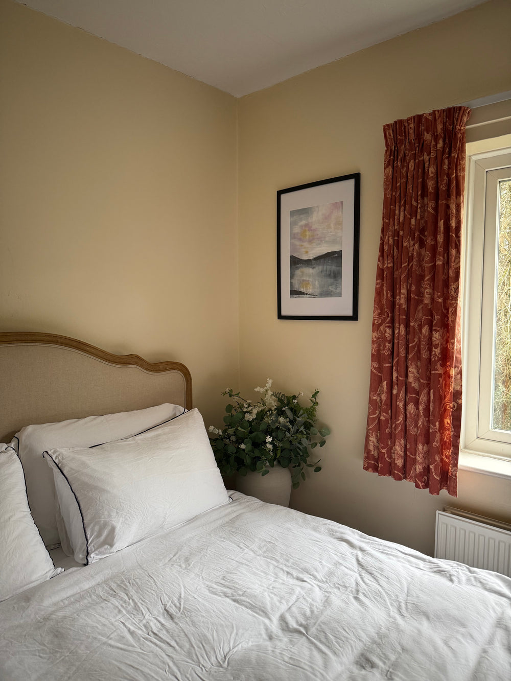 Bedroom with a bed, floral arrangement, and framed picture on the wall.