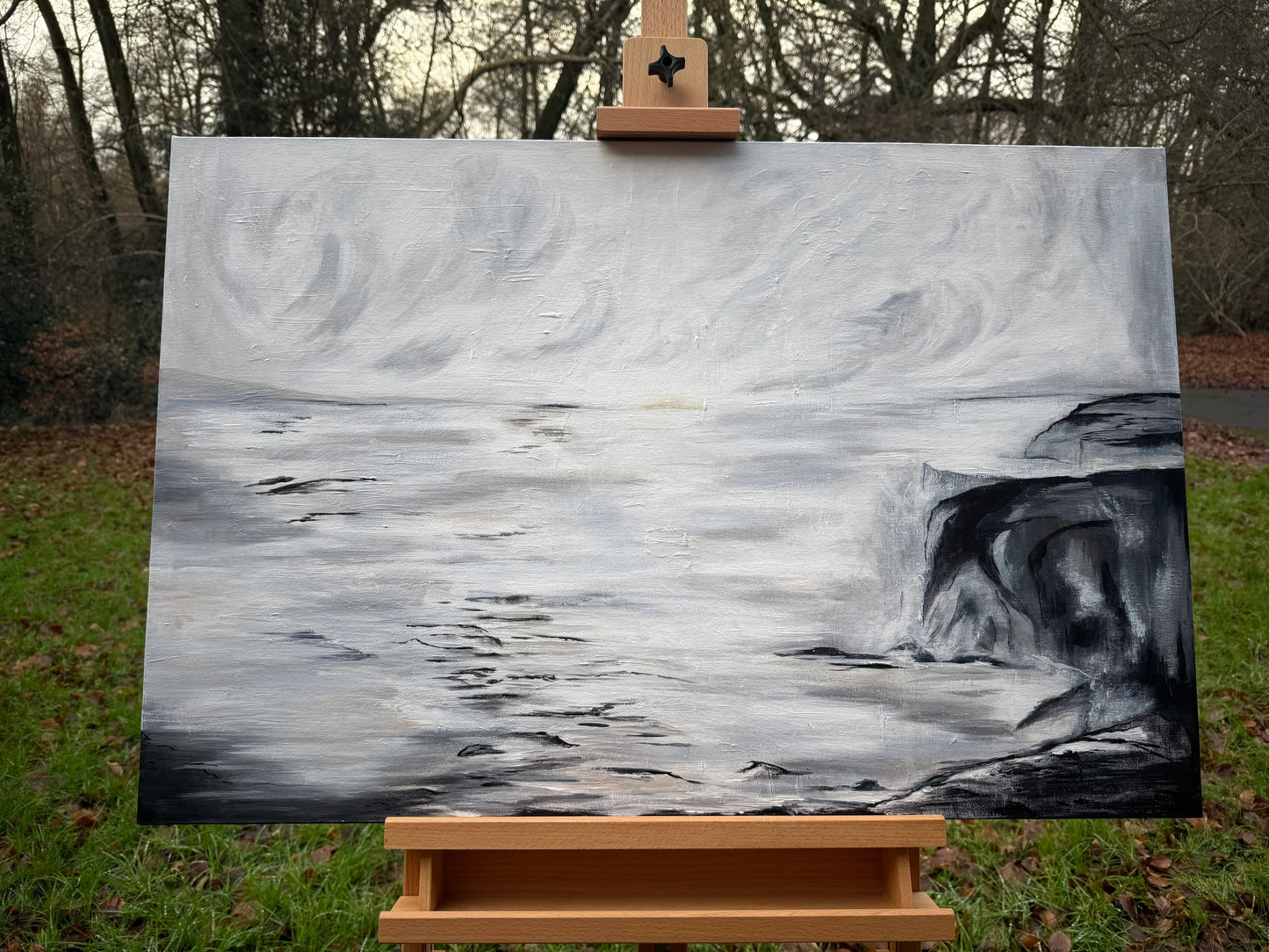 Monochrome oil painting of stormy sea cliffs and swirling sky on artist's easel outdoors