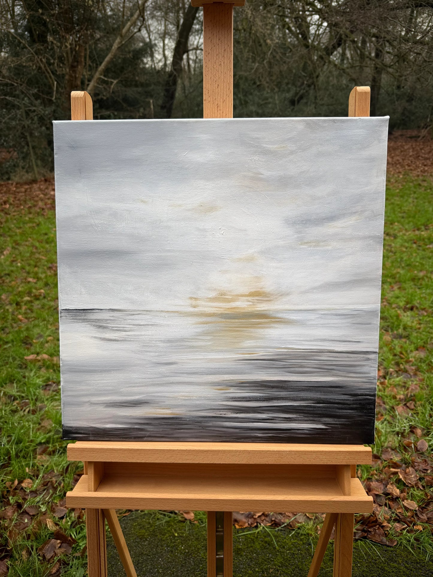 Abstract oil painting of a sunrise over water with soft, muted colors on an easel outdoors.
